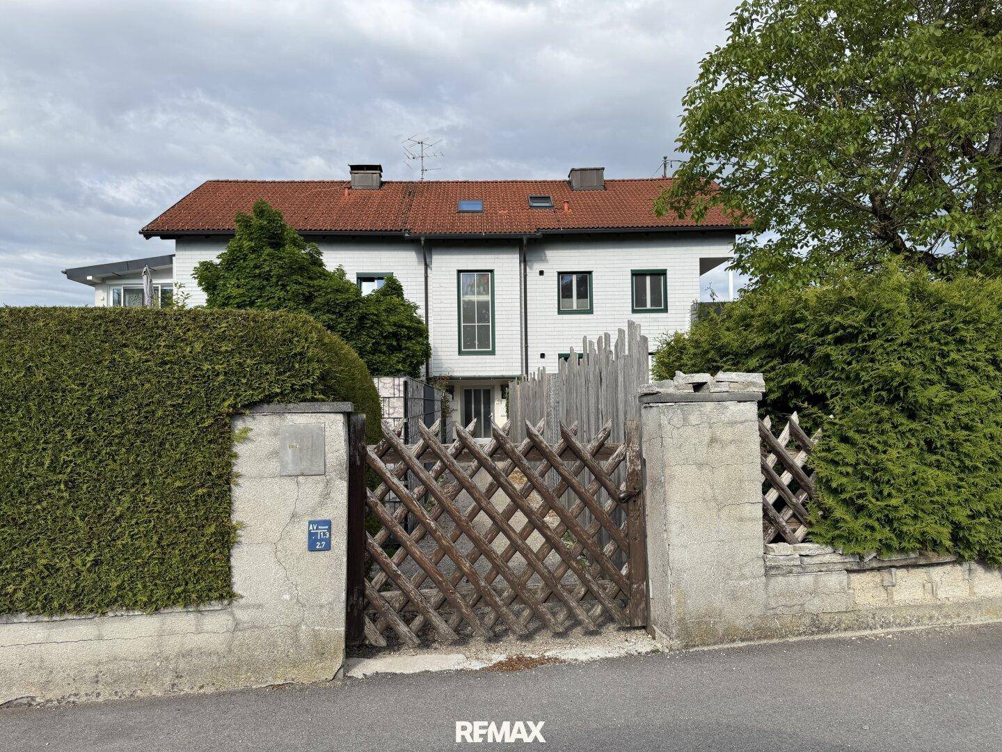 Traditionelles Haus mit weißer Fassade, rotem Ziegeldach und Holzzaun.