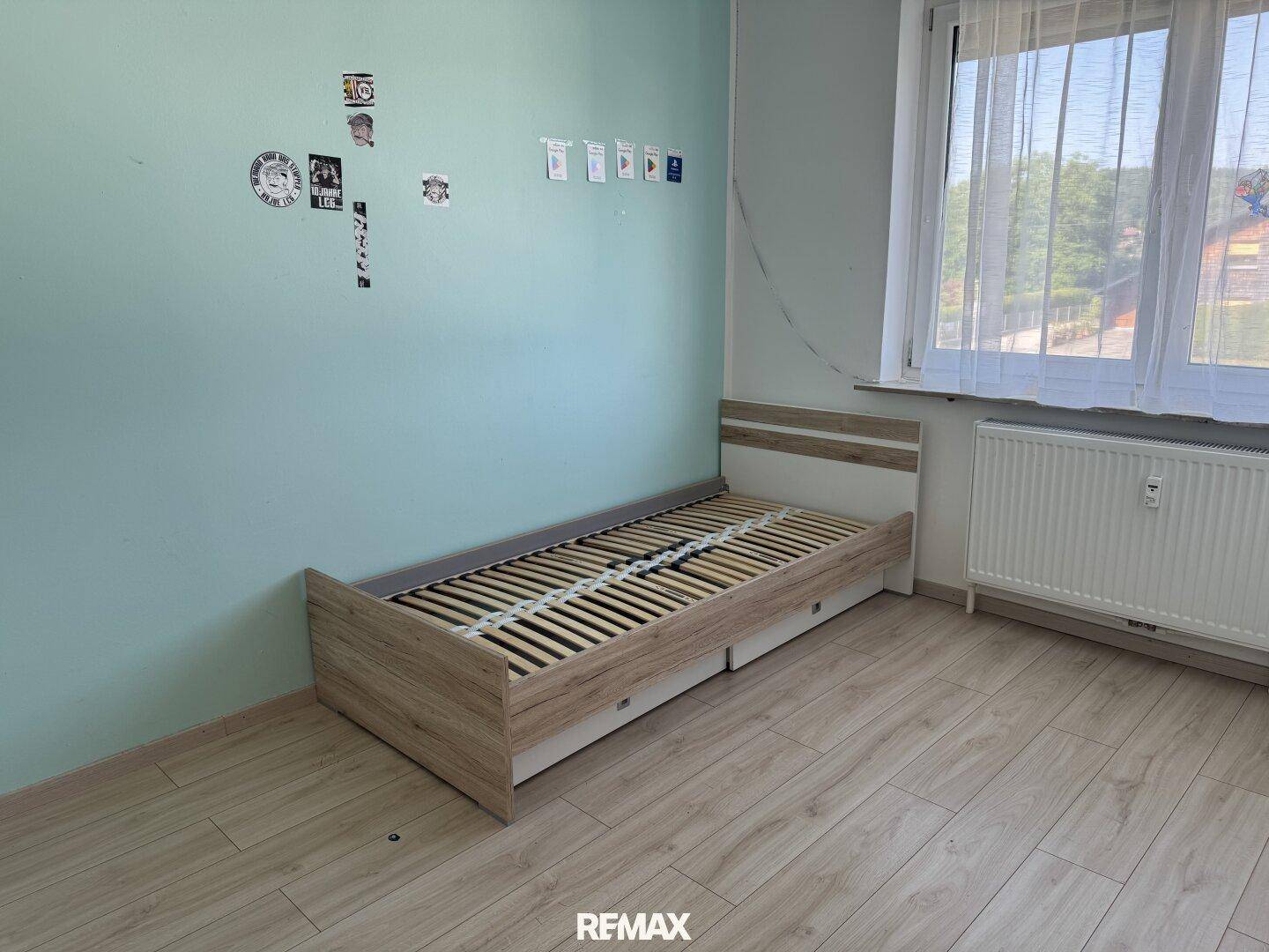 Helles Schlafzimmer mit Einzelbett, Laminatboden und einem Fenster für Tageslicht.