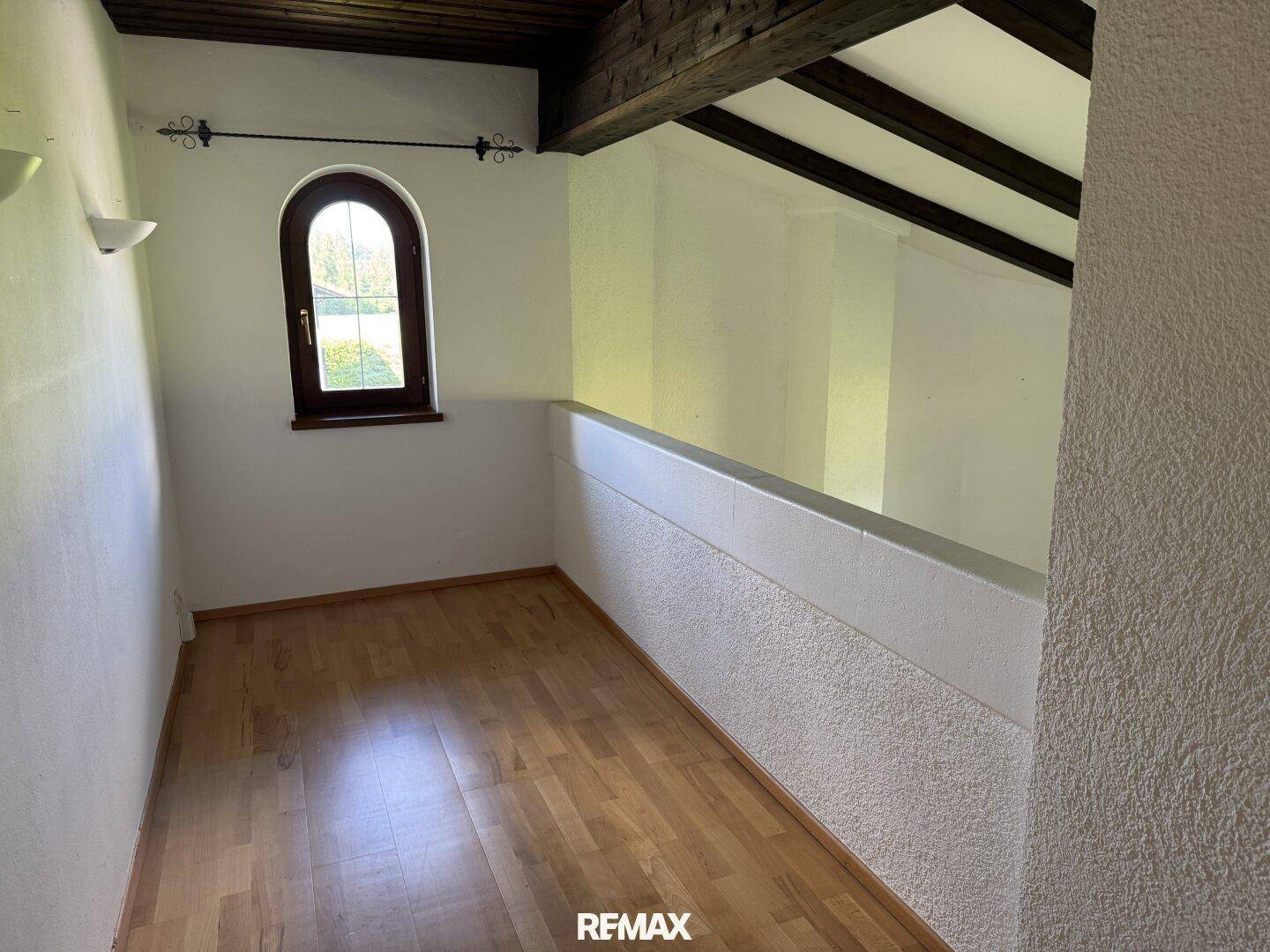 Heller Flur im Obergeschoss mit Holzboden, weiß gestrichenen Wänden und einem Rundbogenfenster.