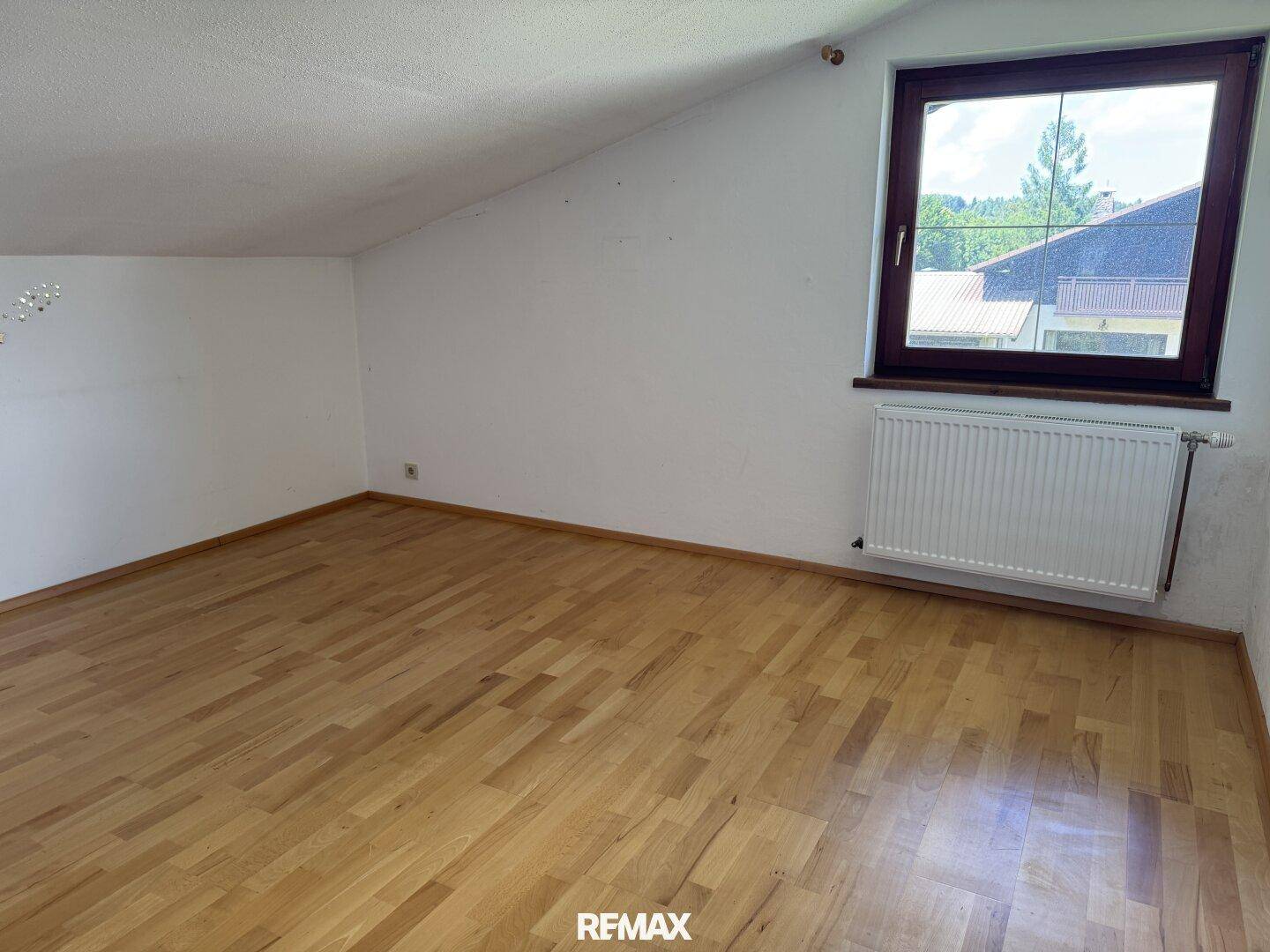Helles Schlafzimmer im Dachgeschoss mit Holzboden, Fenster und Heizkörper unter der Schräge.