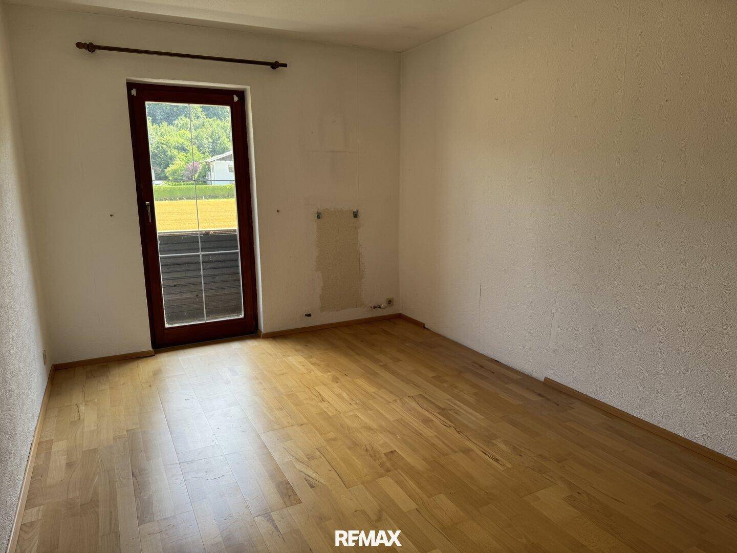 Schlafzimmer mit Holzboden und einer Terrassentür, die viel Tageslicht hereinlässt.