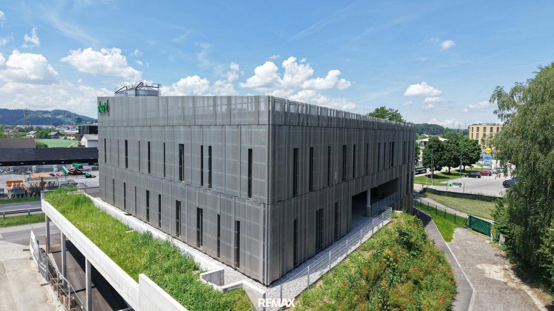 Drohnenansicht des modernen Bürogebäudes mit grüner Dachterrasse und umliegender Landschaft.