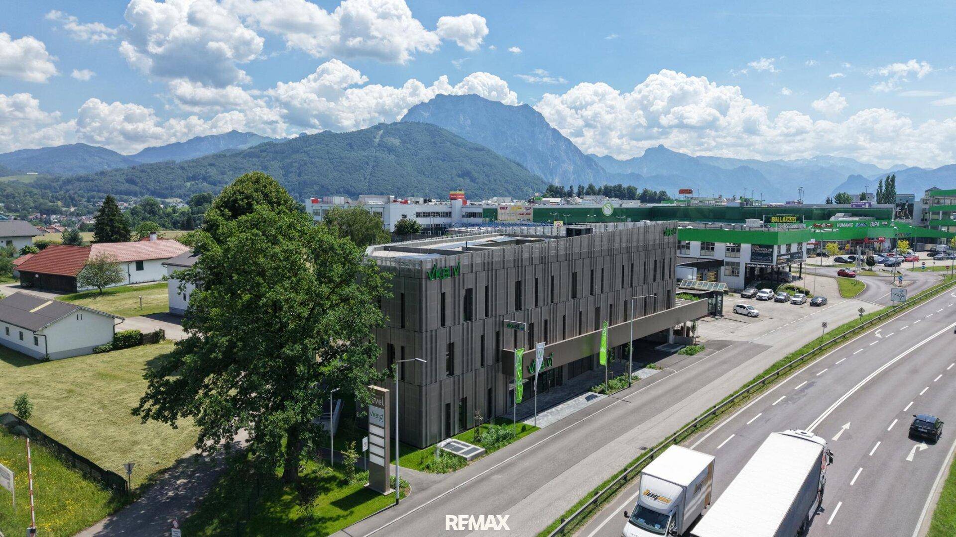 Luftaufnahme eines modernen Geschäftsgebäudes an einer Straße mit Bergen im Hintergrund.