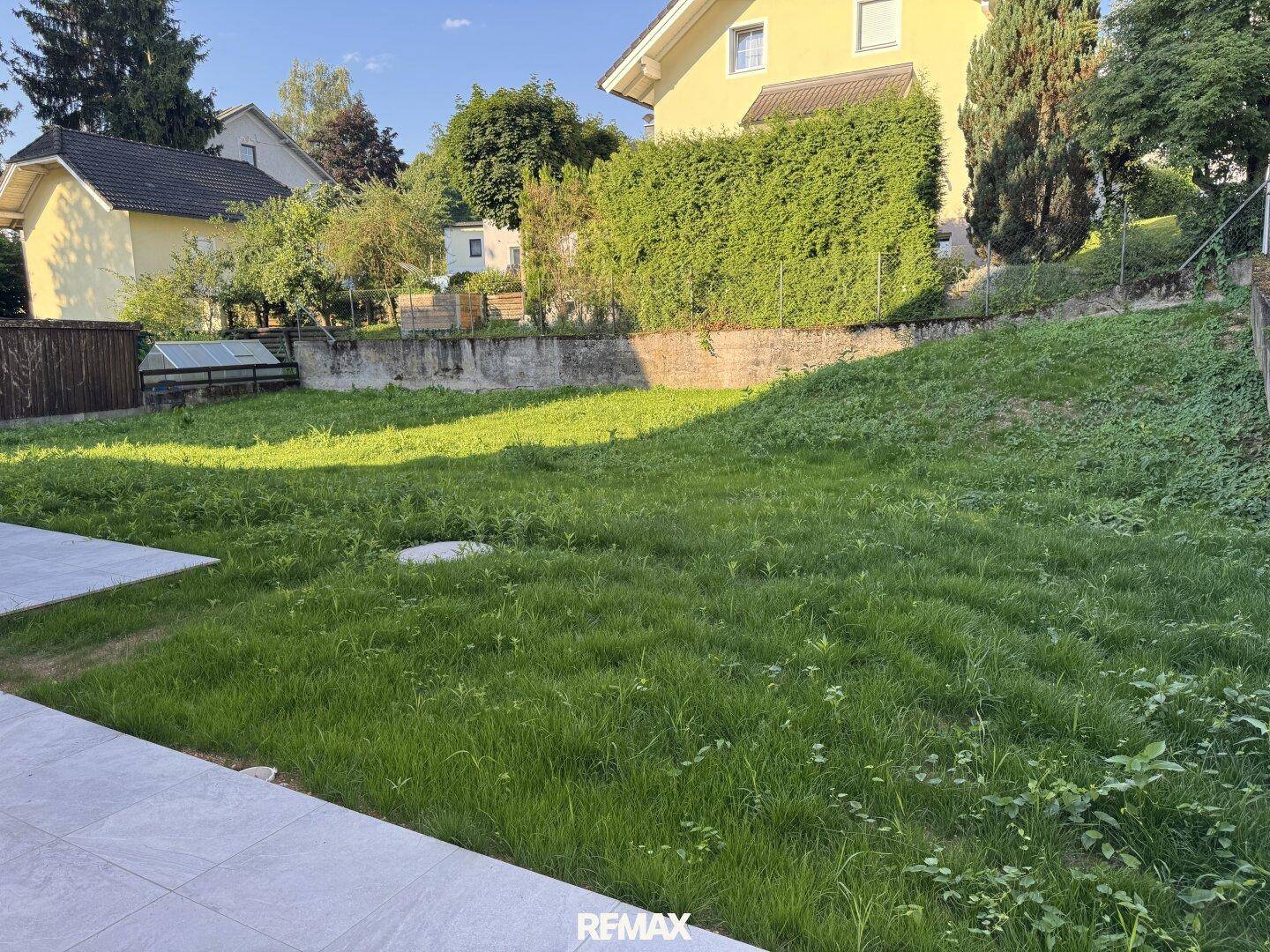 Großer, ungestalteter Gartenbereich mit Rasenfläche und angrenzender Terrasse bei Sonnenschein.