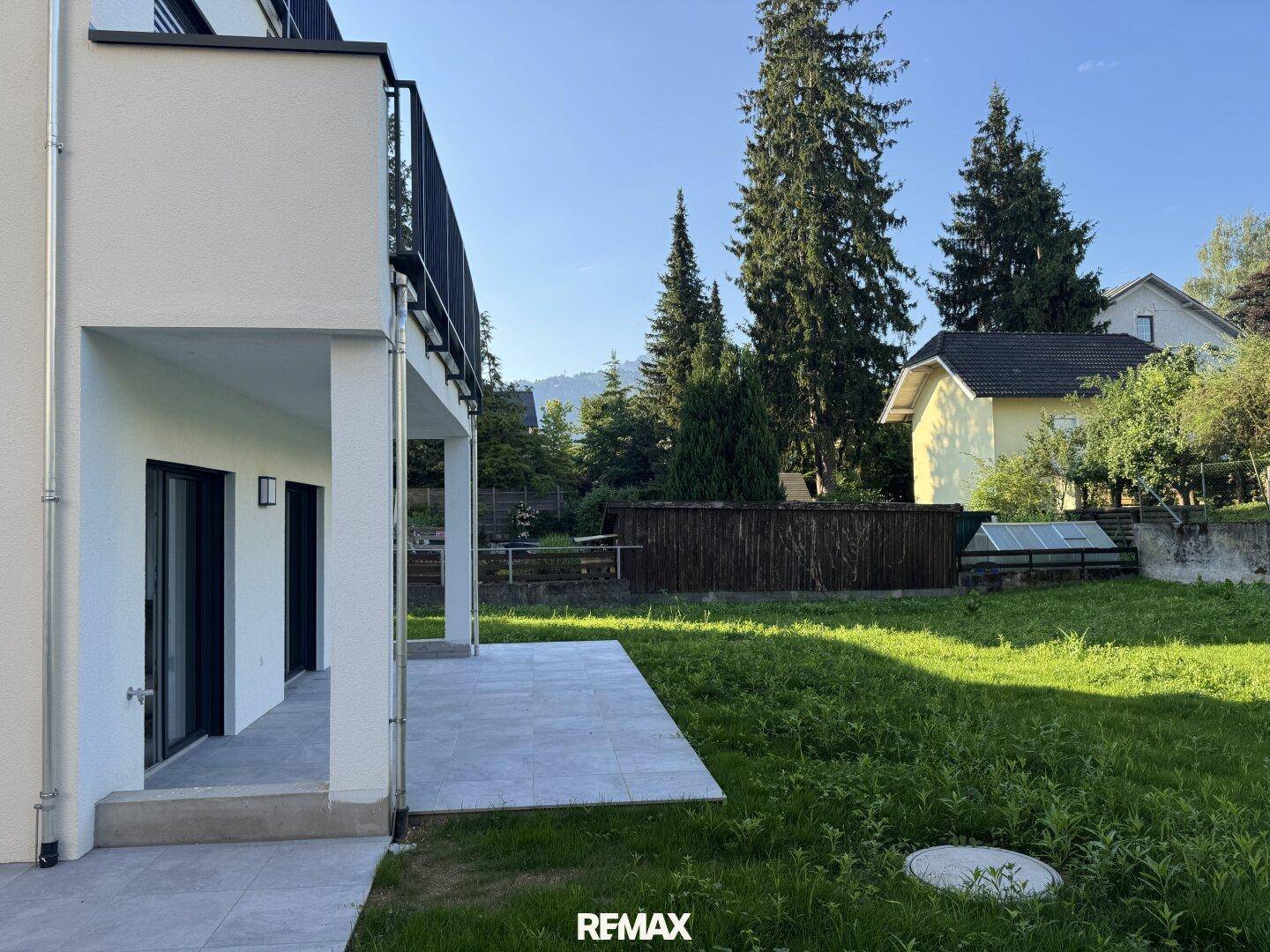 Seitliche Ansicht des Gebäudes mit großer Terrasse und weitläufigem Garten unter blauem Himmel.