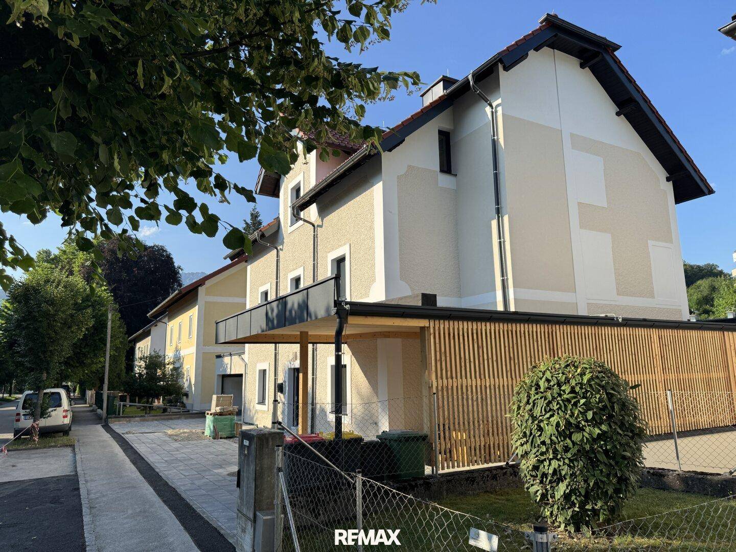 Ansicht des Neubaus von der Straße mit Carport und moderner Fassade an einem sonnigen Tag.