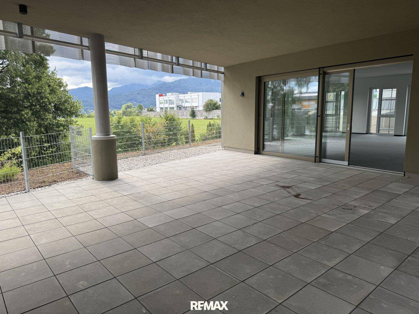 Große gepflasterte Terrasse mit Überdachung und Blick auf die Berge, direkt zugänglich vom Innenbereich.