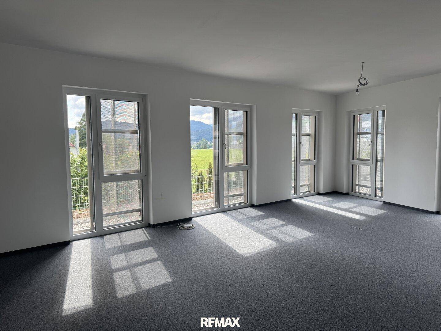 Heller Büroraum mit grauem Teppichboden, durchflutet von natürlichem Licht, mit Blick ins Grüne.