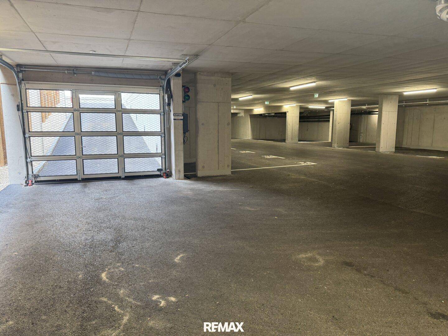 Geräumige Tiefgarage mit vielen Stellplätzen, Betonstützen und einem Rolltor am Eingang.