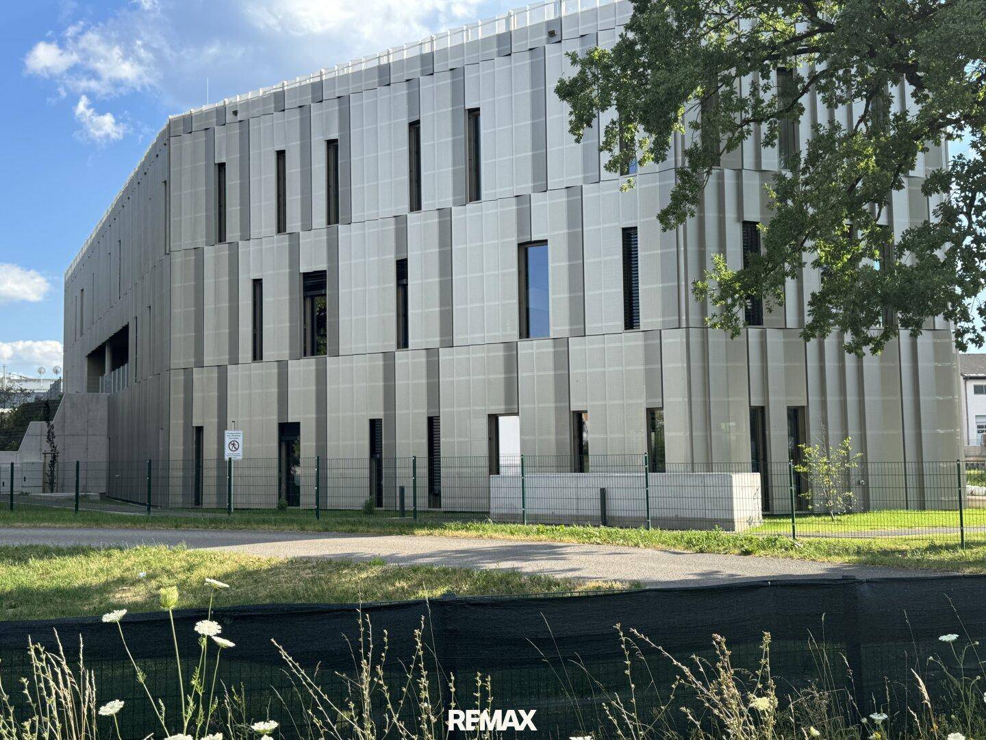 Seitenansicht des modernen Bürogebäudes mit strukturierter Fassade und umzäunter Grünfläche.
