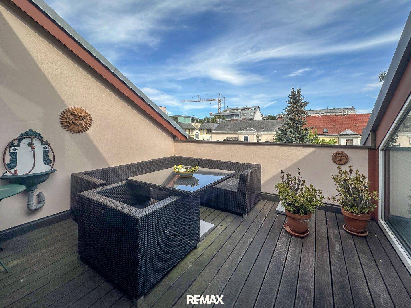 Gemütliche Dachterrasse mit Holzboden und Loungemöbeln unter blauem Himmel.