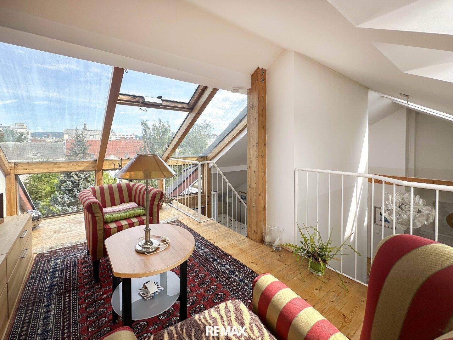 Helles Wohnzimmer im Dachgeschoss mit großen Fenstern, Holzbalken und Blick ins Grüne.