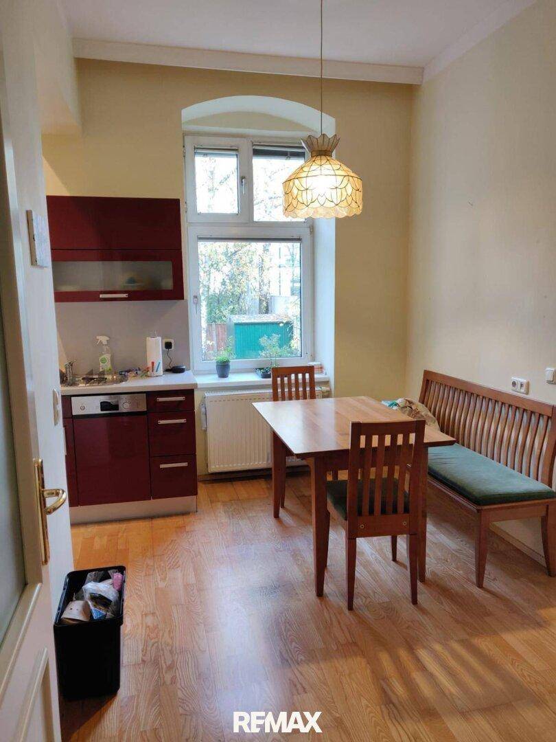Gemütliche Wohnküche mit roten Unterschränken, einem Holztisch mit Stühlen und einer Sitzbank am Fenster.