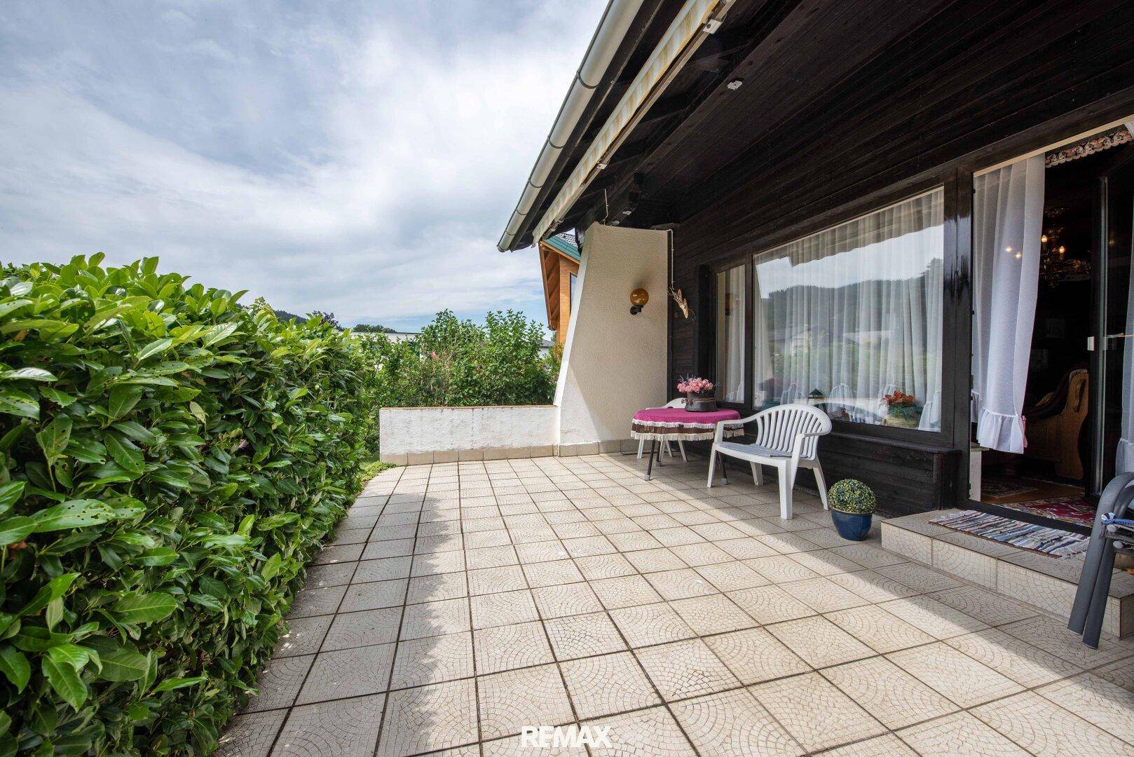 Geflieste Terrasse mit Gartenmöbeln und einer hohen Hecke, die Privatsphäre bietet.