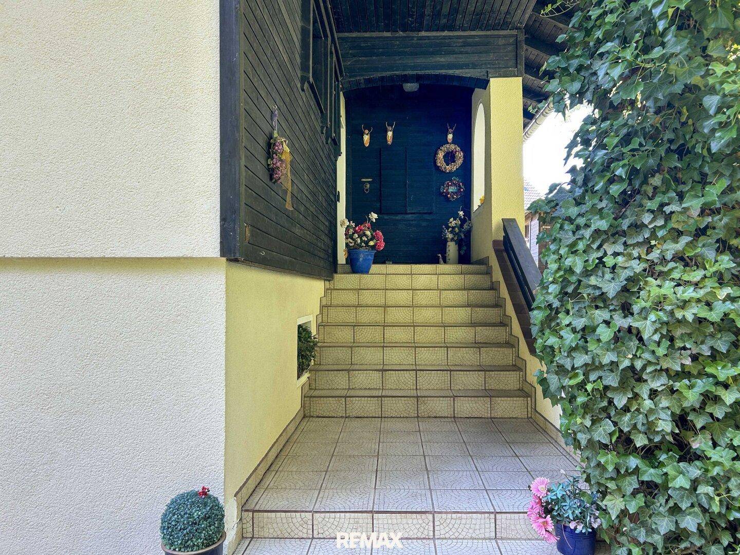 Eingangsbereich des Hauses mit gefliesten Stufen und traditioneller Dekoration an der Tür.