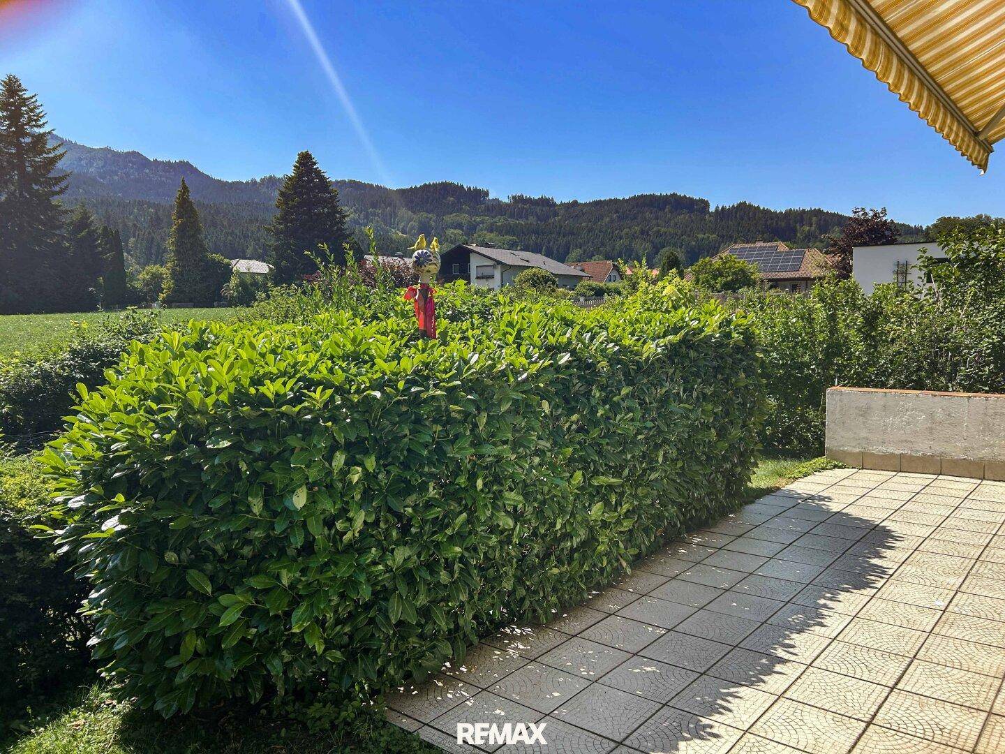 Sonniger Terrassenbereich mit Hecke und weitem Blick auf die umliegende Landschaft.