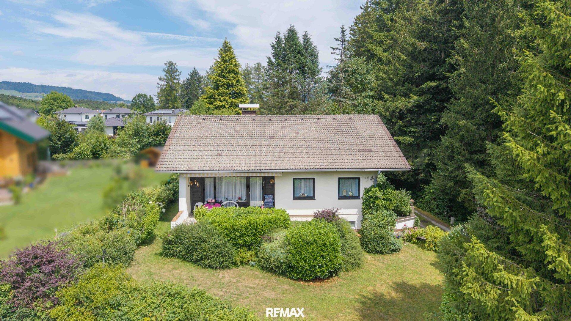 Luftaufnahme eines Einfamilienhauses mit Garten, umgeben von Bäumen und grüner Landschaft.