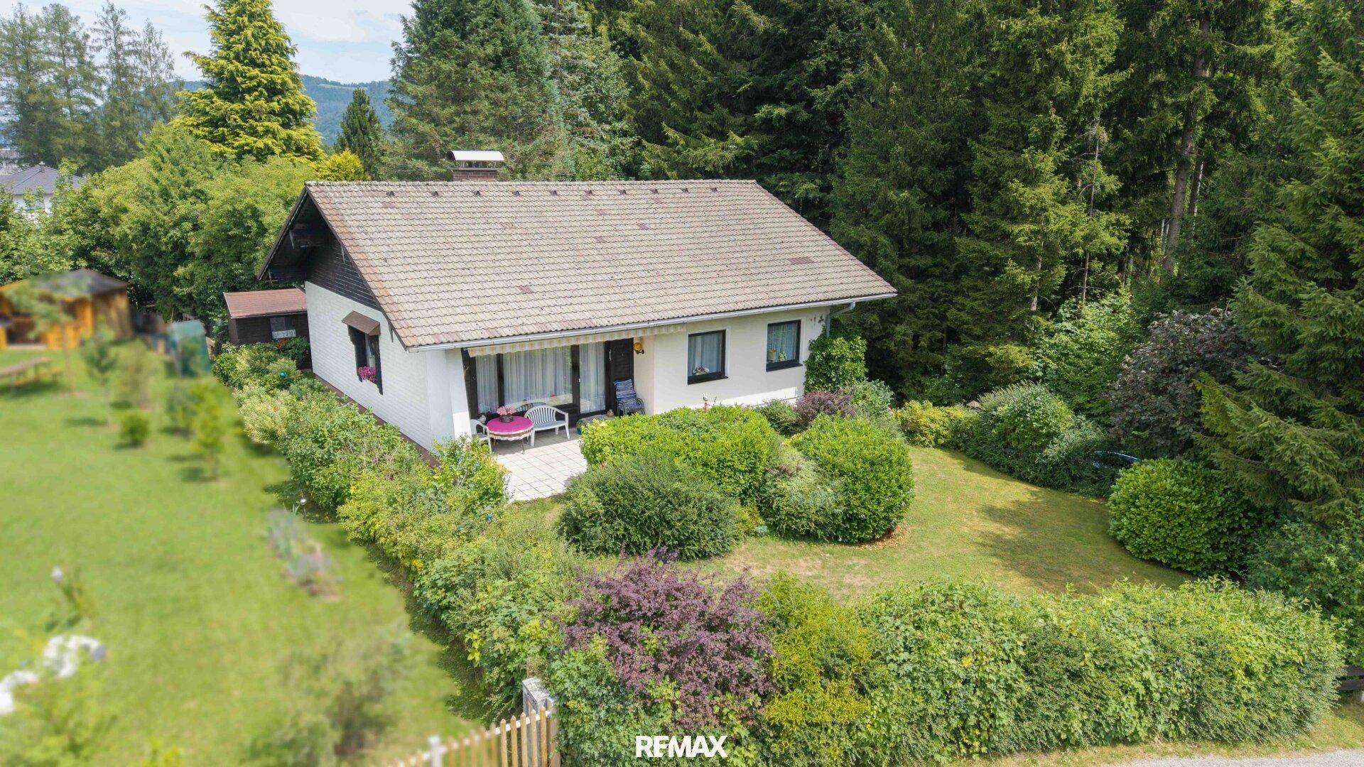 Luftaufnahme eines Einfamilienhauses mit Garten, umgeben von Bäumen und grüner Landschaft.