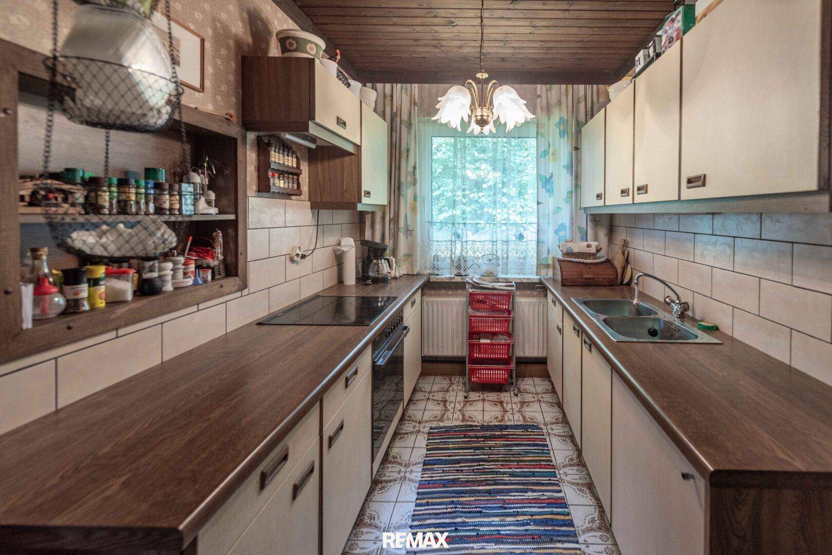 Schmale Küche im Landhausstil mit Holzdecken, Fliesenboden und Fenster zum Garten.