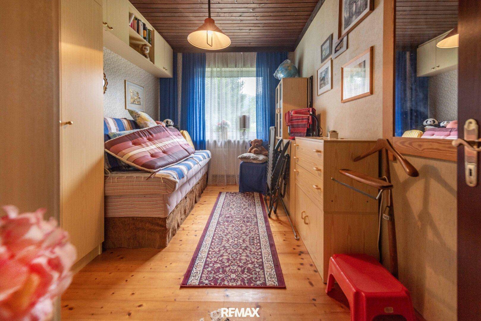 Kleines Schlafzimmer oder Gästezimmer mit Holzfußboden, Einzelbett und blauen Vorhängen.