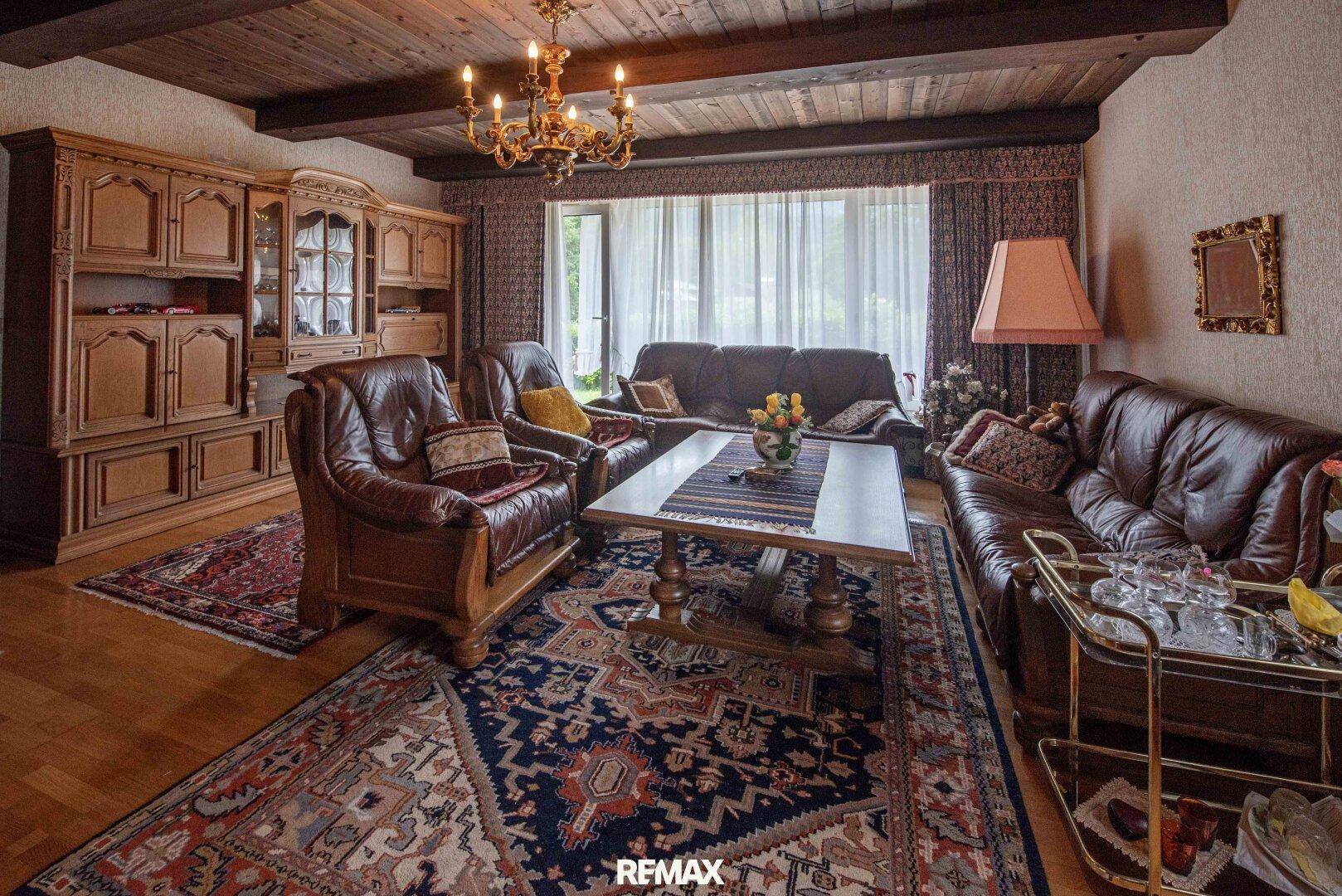 Geräumiges Wohnzimmer mit Ledersofas, Holzmöbeln und großem Fenster mit Vorhängen.