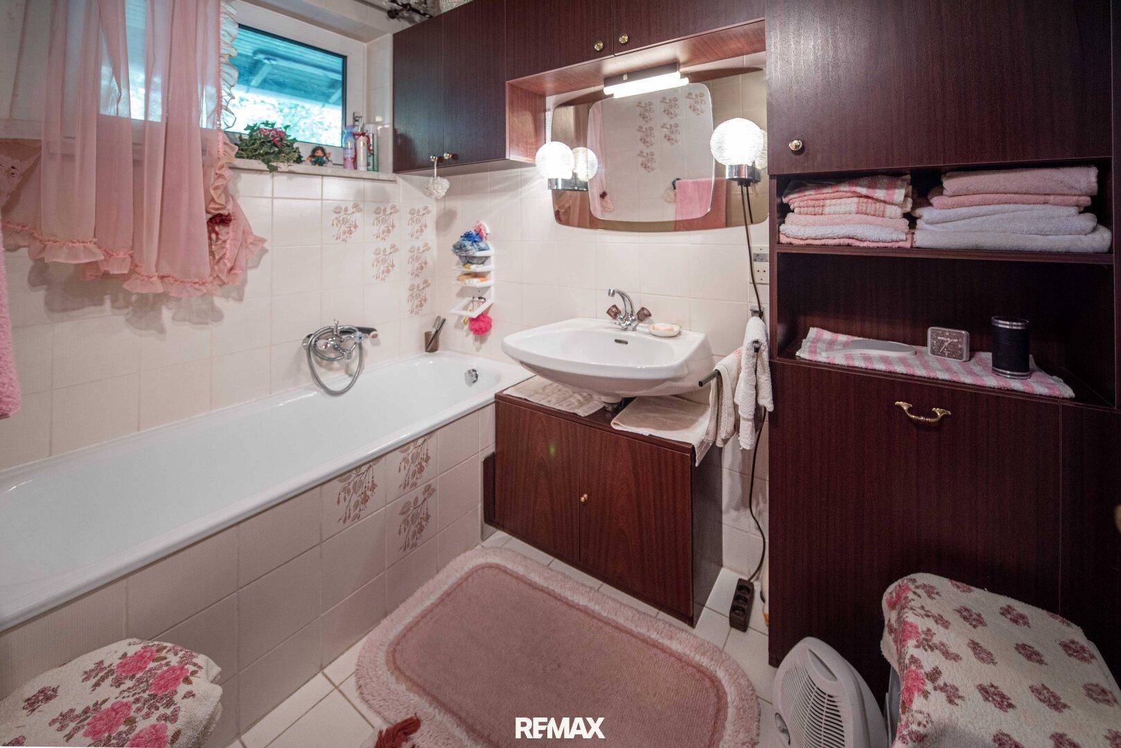 Badezimmer im Stil der 80er Jahre mit Badewanne, Waschbecken und rosa Vorhängen.