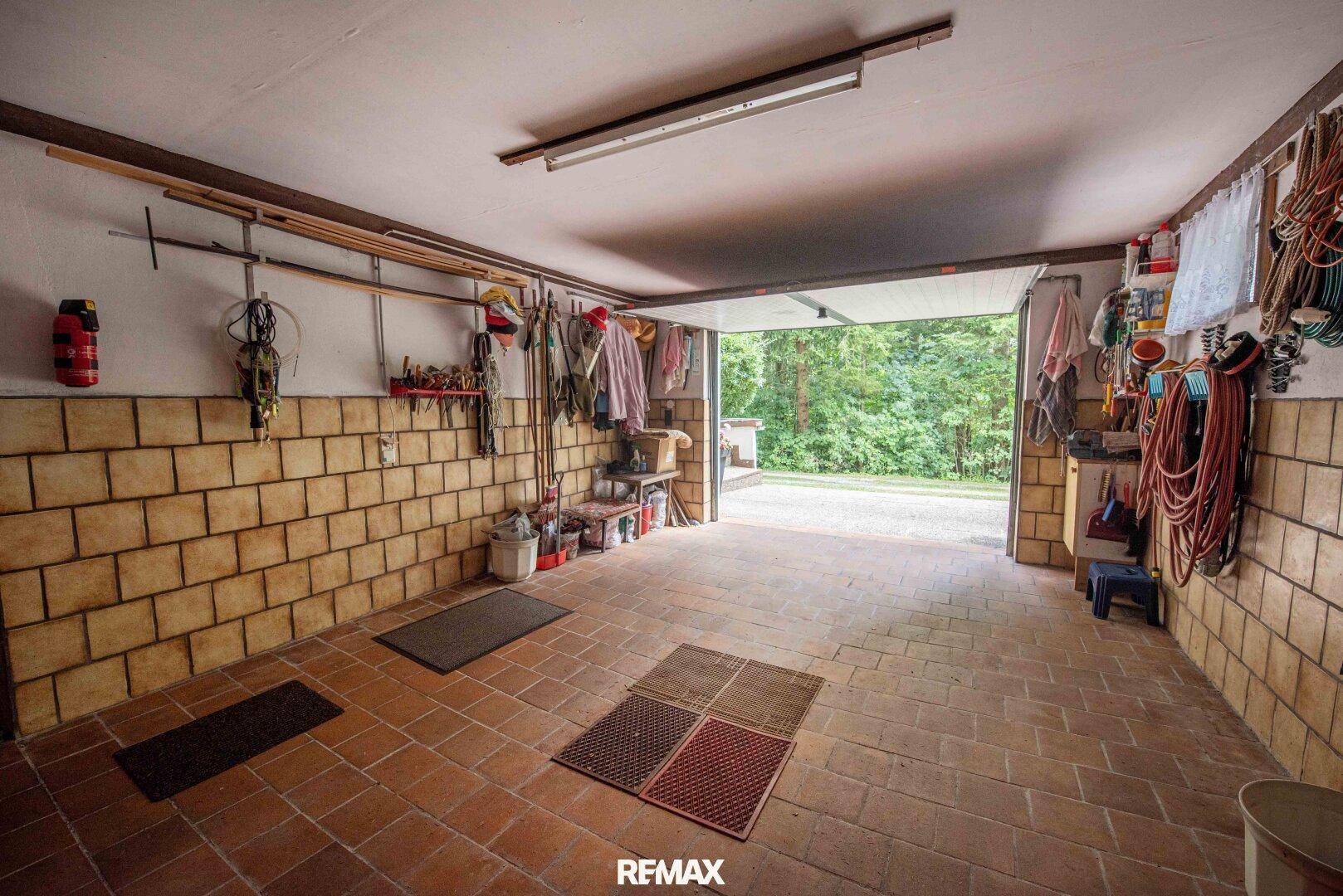 Geräumige Garage mit gefliesten Wänden und Boden, genutzt als Werkstatt und Abstellraum.