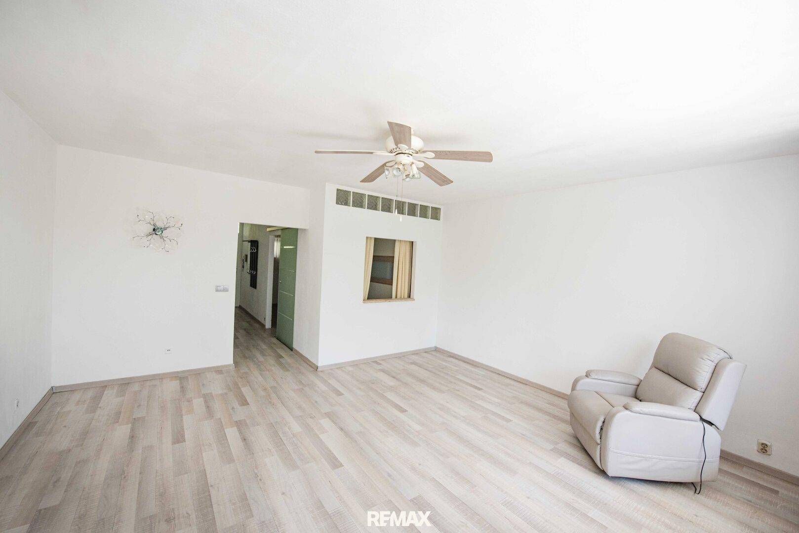 Helles Wohnzimmer mit hellem Laminatboden und Deckenventilator, bereit zur individuellen Gestaltung.