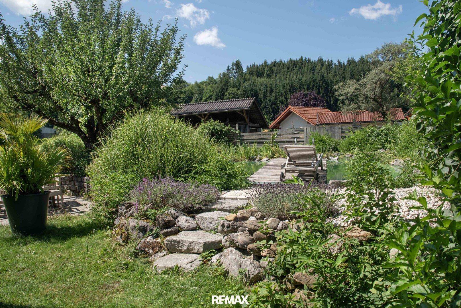 Idyllischer Gartenbereich mit Natursteintreppe, üppiger Bepflanzung und einem Teich im Hintergrund.