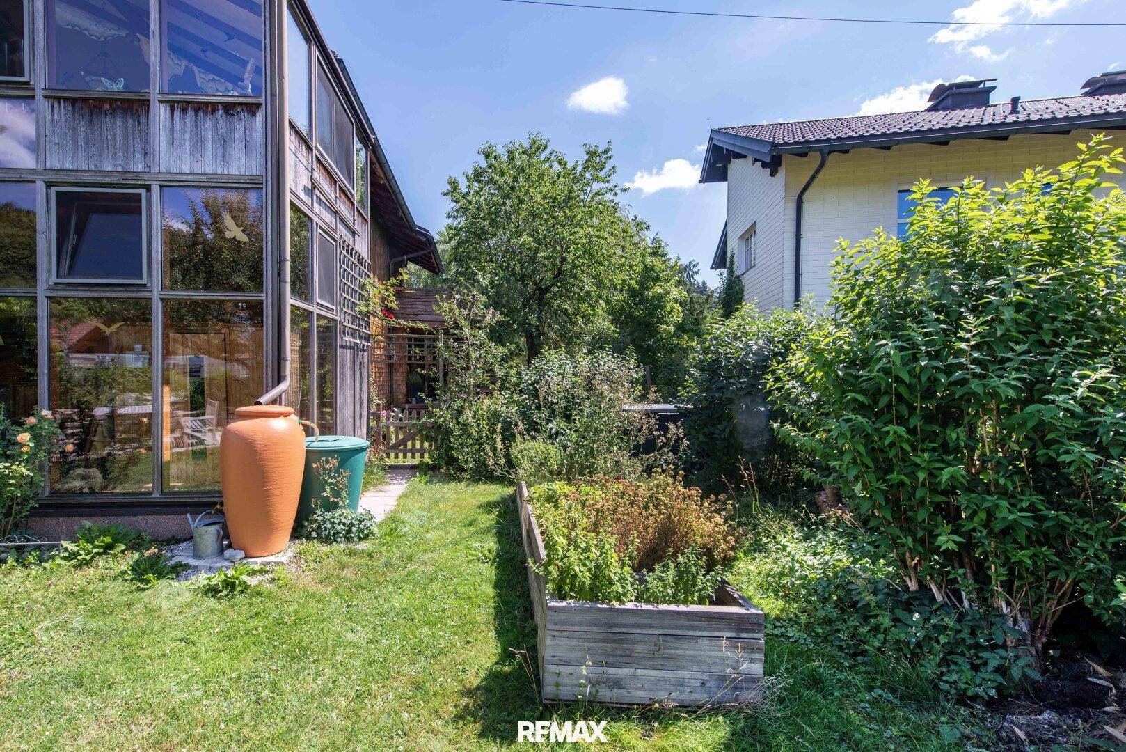 Kleiner Küchengarten mit Hochbeet neben der Glasfassade des Hauses, umgeben von Grünflächen.