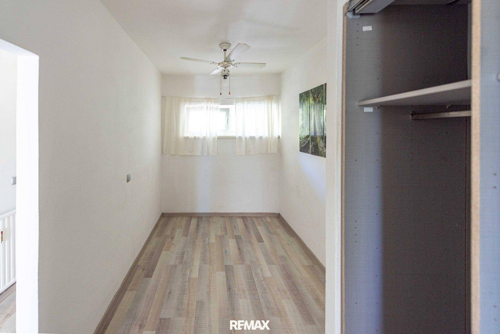 Heller Raum mit Laminatboden, Deckenventilator und integriertem Kleiderschrank.