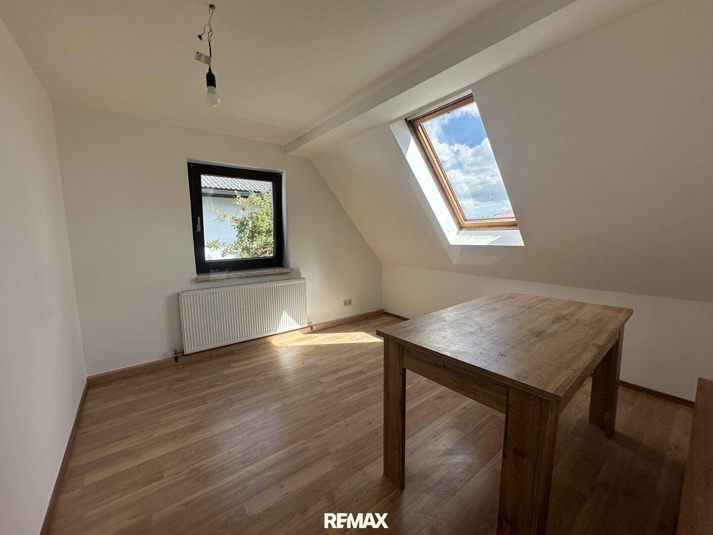 Heller Raum mit Laminatboden, Dachschräge, Dachfenster und einem Holztisch.