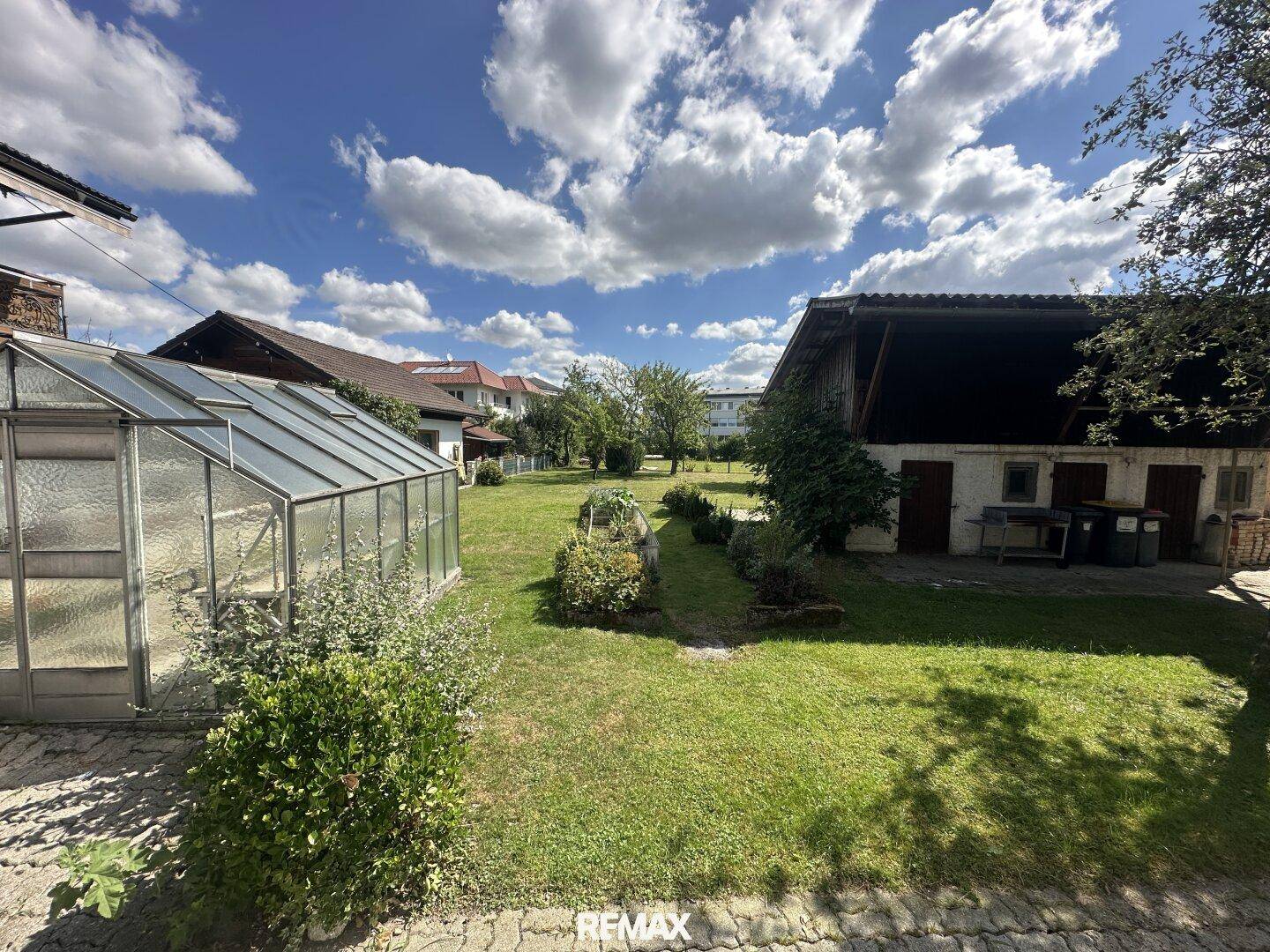 Hinterhof mit Gewächshaus, Gartenbeeten und einem Nebengebäude.
