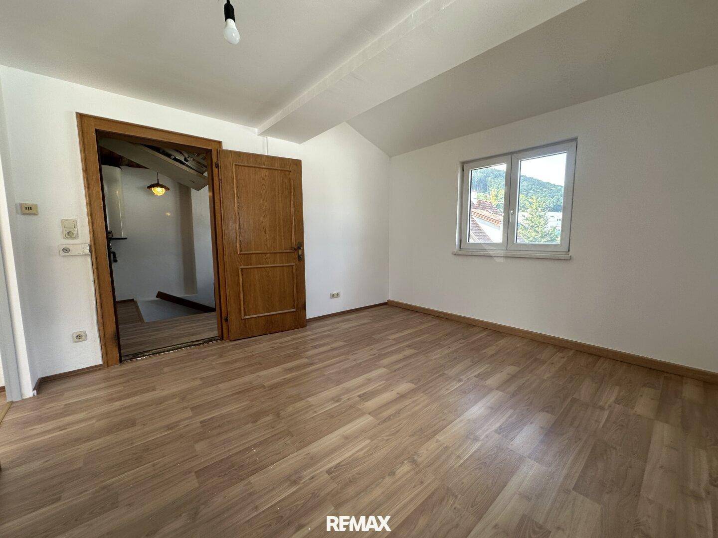 Geräumiger Raum mit Laminatboden, Dachschräge und Holztür zu einem weiteren Bereich.