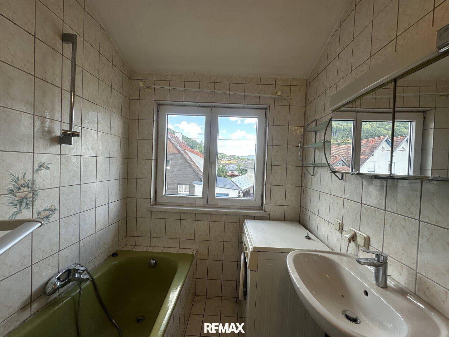 Badezimmer mit grüner Badewanne, weißen Fliesen, Einzelwaschbecken und Fenster.