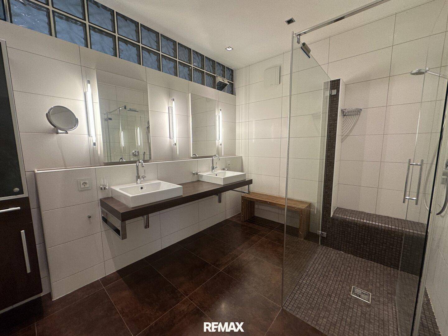 Modernes Badezimmer mit Doppelwaschbecken, großer begehbarer Dusche und Fliesenboden.