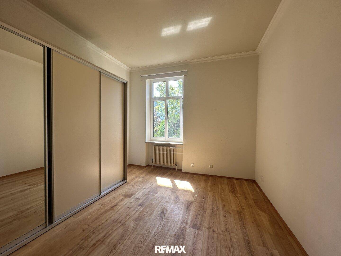 Helles Schlafzimmer mit Holzfußboden, großem Spiegelschrank und viel natürlichem Licht.
