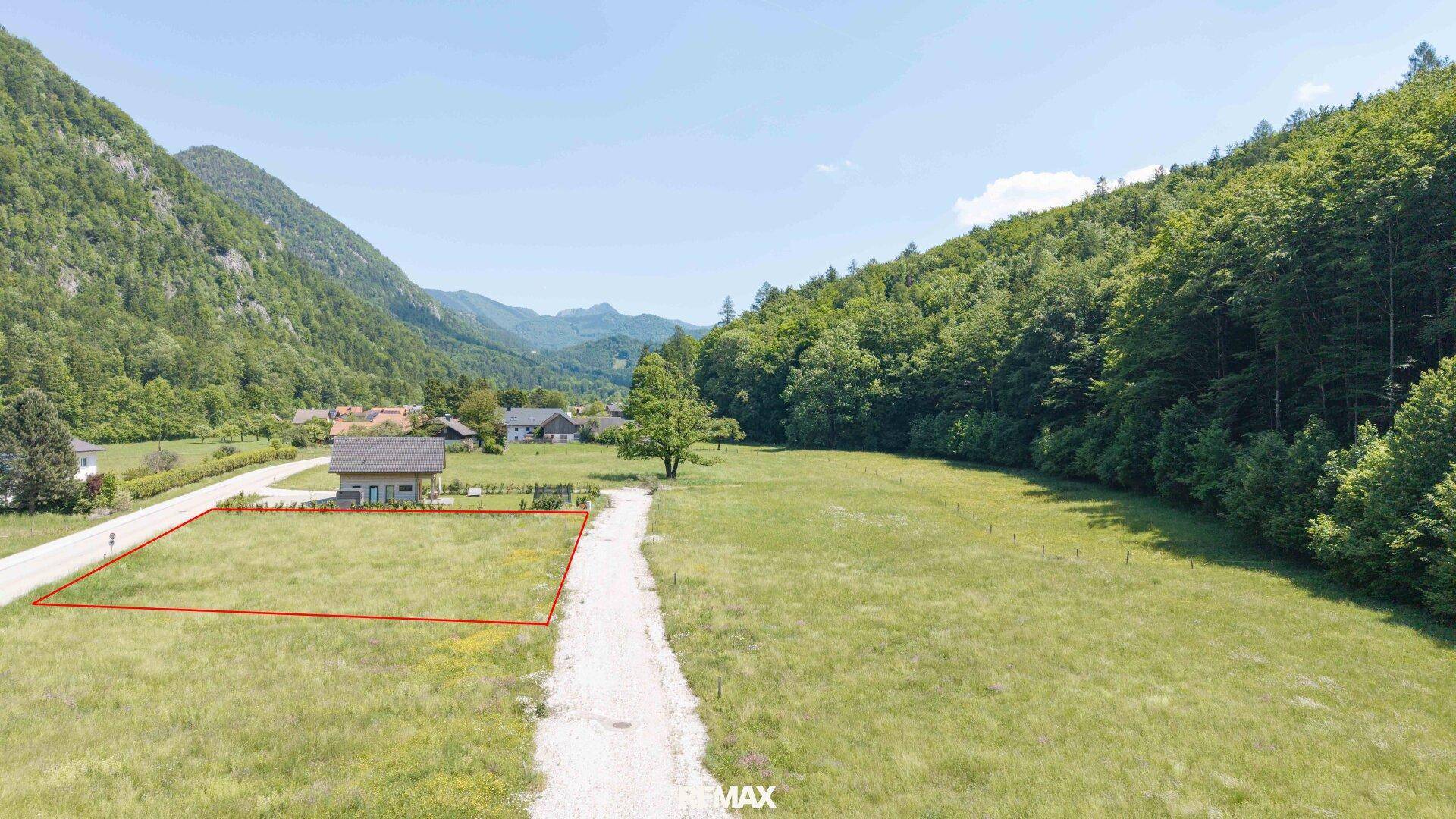 Luftaufnahme eines umgrenzten Grundstücks in einer malerischen Berglandschaft mit Wiesen und Wäldern.