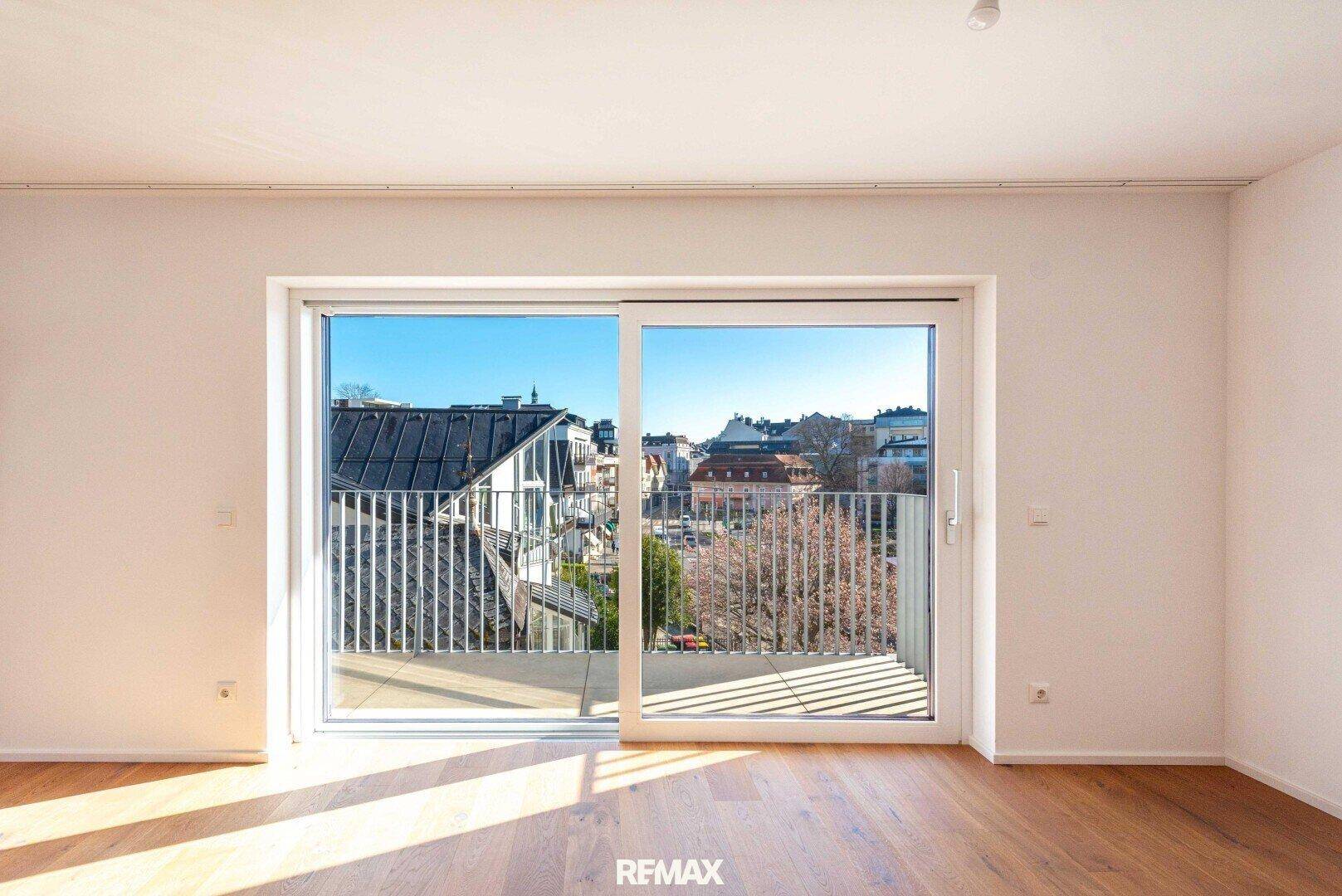 Helles Wohnzimmer mit Holzboden, großem Schiebefenster und Blick auf die Stadt.