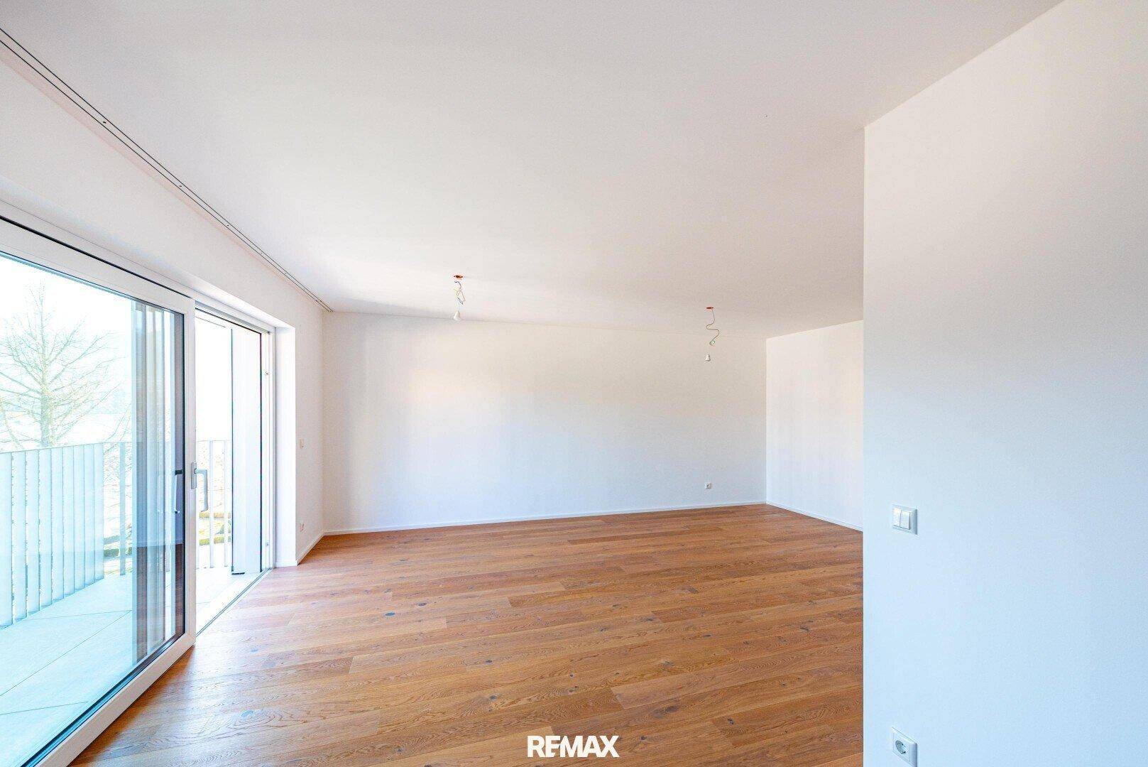 Geräumiges, lichtdurchflutetes Wohnzimmer mit Holzboden und Zugang zum Balkon.