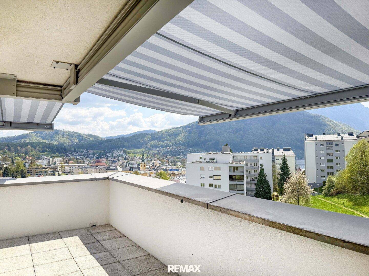 Sonniger Terrassenbereich mit ausgefahrener Markise und Panoramablick auf See und Berge.