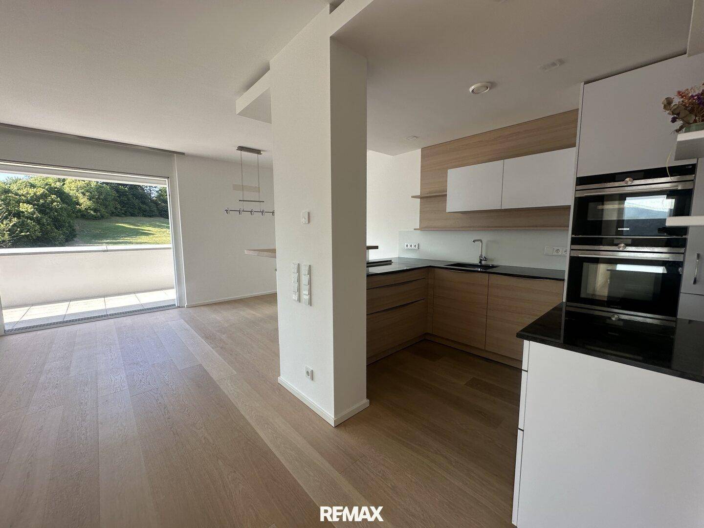 Moderne Einbauküche mit Holzfronten, schwarzen Arbeitsplatten und integrierten Geräten.