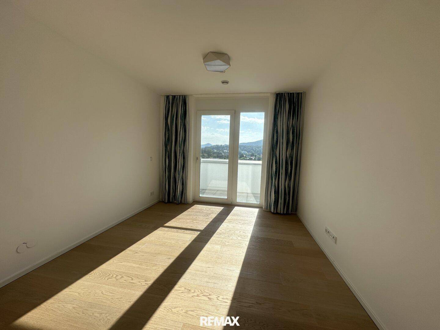Schlafzimmer mit Holzparkettboden und direktem Zugang zu einem sonnigen Balkon oder einer Terrasse.