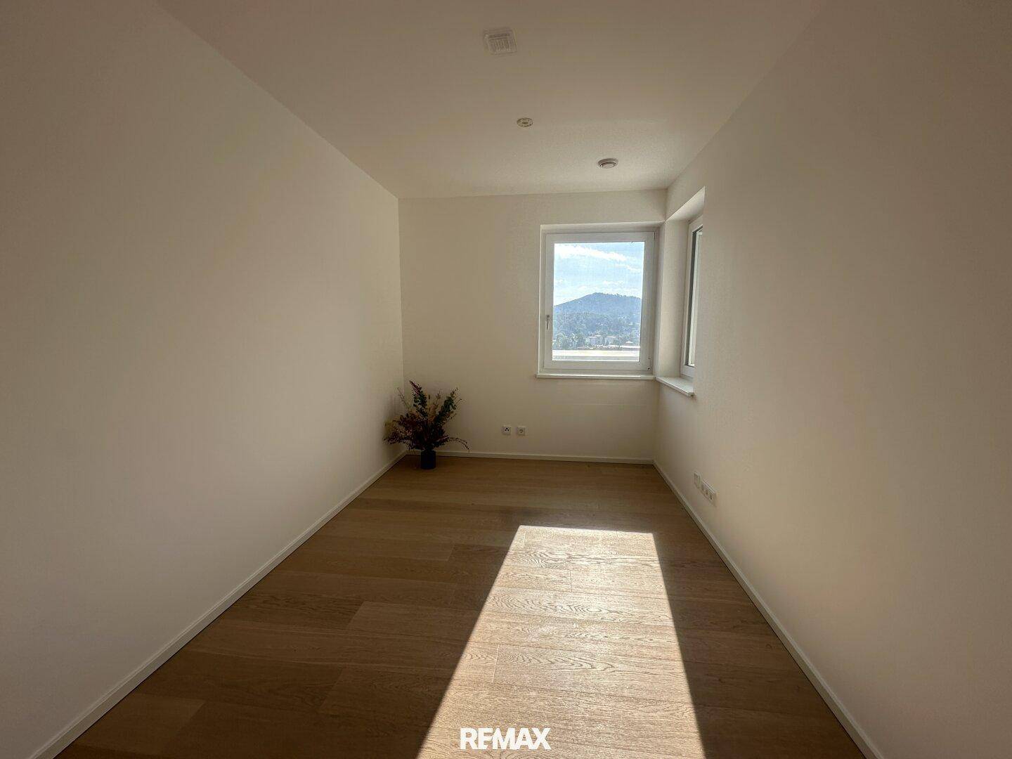 Helles Zimmer mit Holzparkettboden und einem Fenster mit Blick auf die umliegende Landschaft.