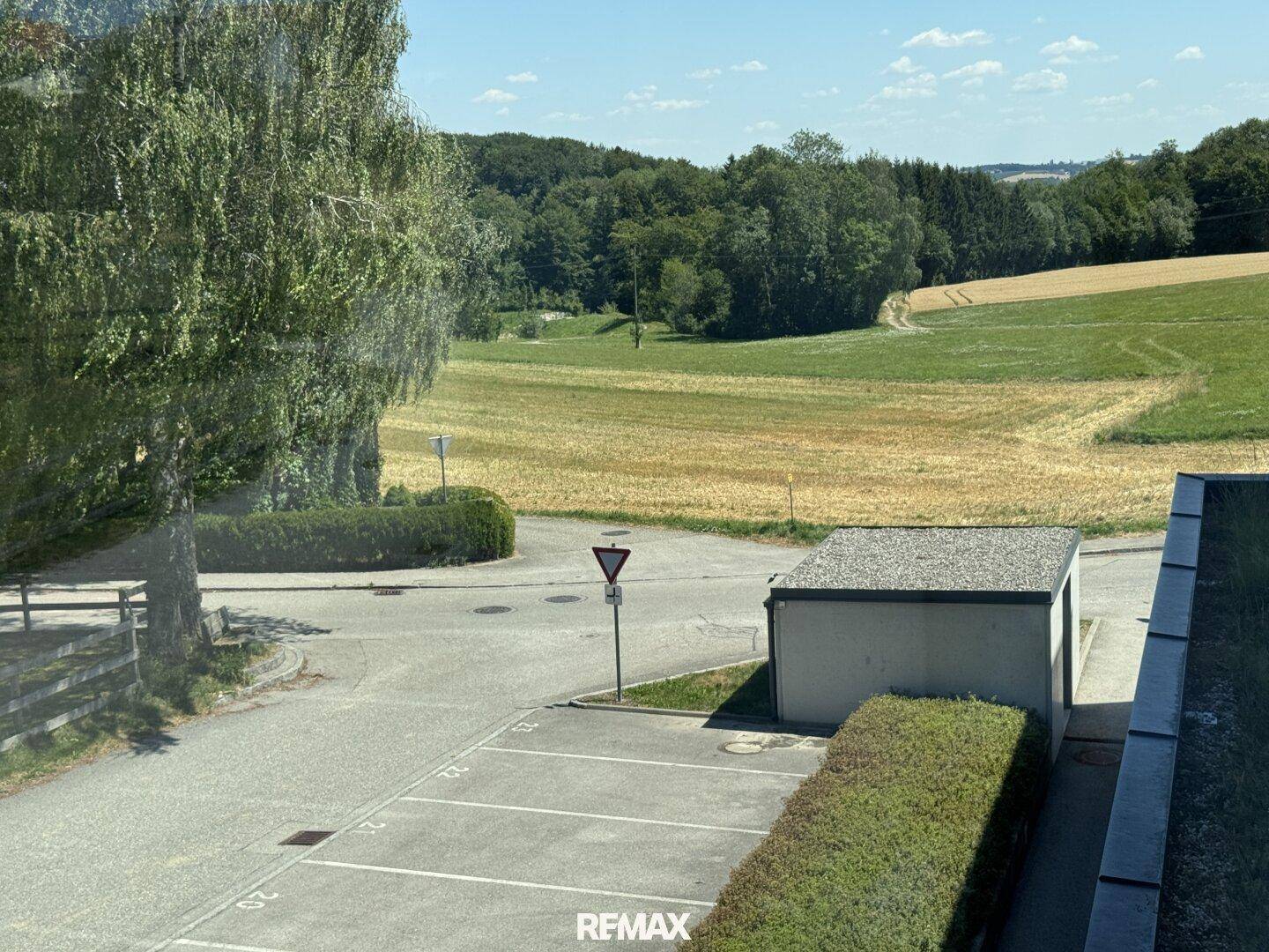Weitläufiger Blick auf Felder, Bäume und eine Straße mit Parkplätzen.
