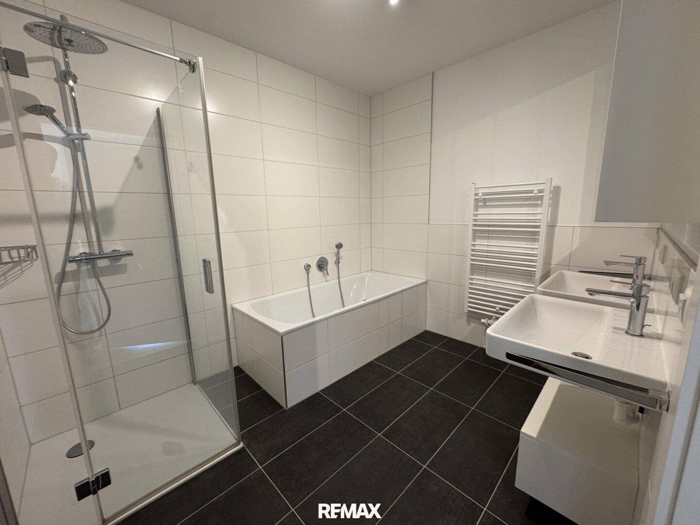Modernes Badezimmer mit Badewanne, begehbarer Dusche, Doppelwaschbecken und weißen Fliesen.
