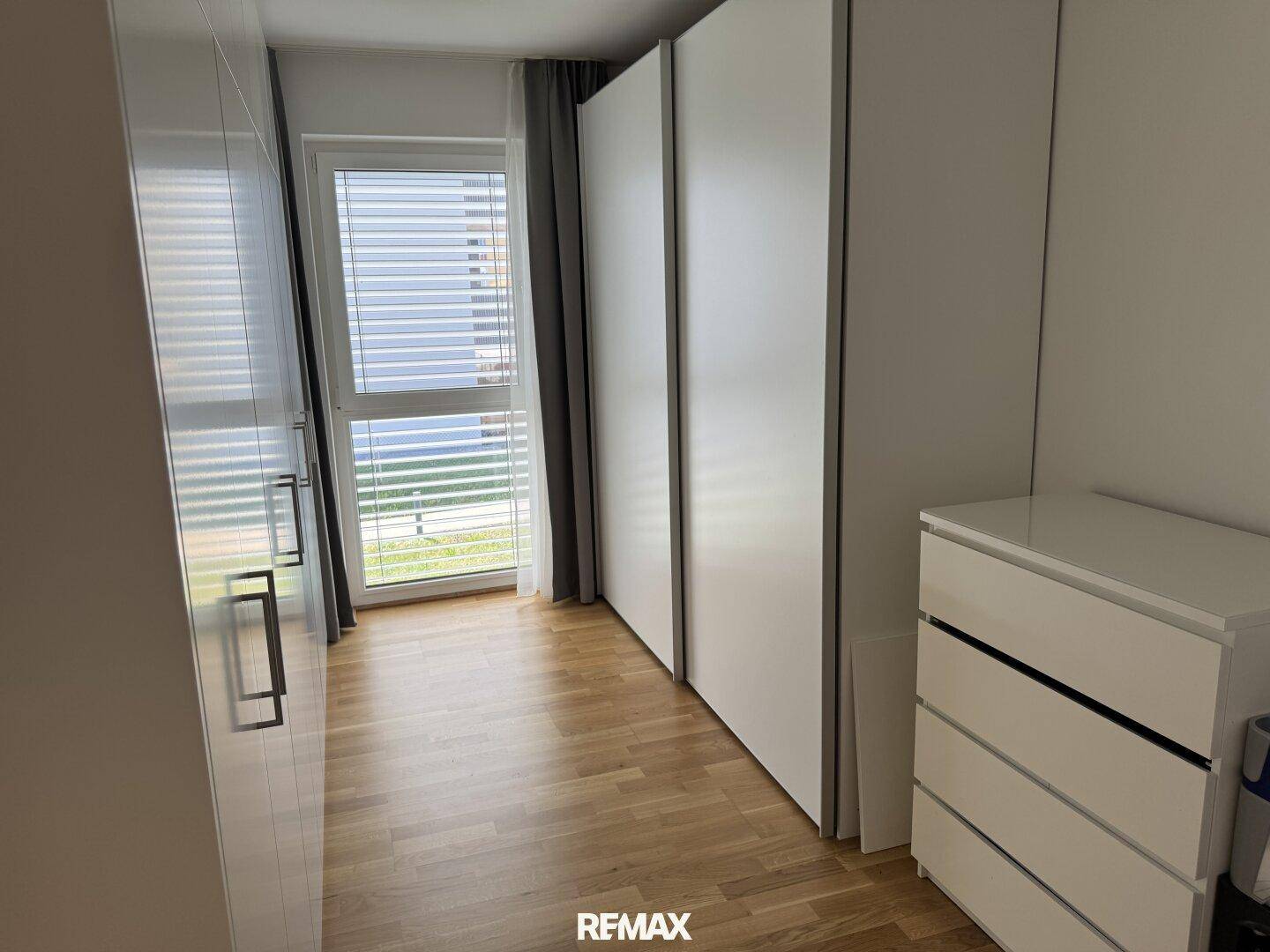 Schlafzimmer mit Holzparkettboden, Einbauschränken und Fenster mit Jalousien.