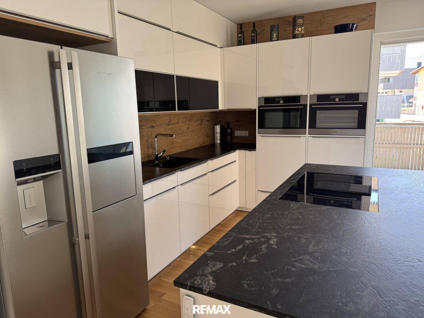 Moderne Einbauküche mit weißen Hochglanzfronten, dunkler Arbeitsplatte und integrierten Geräten.