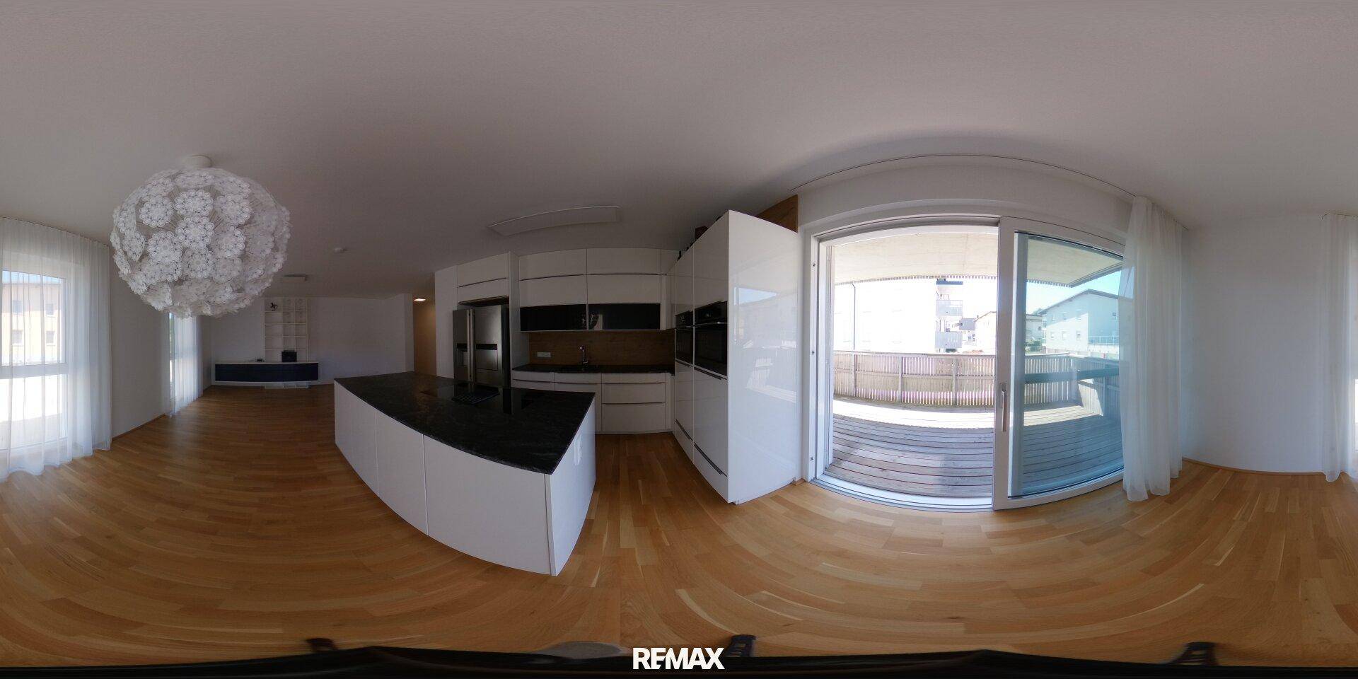 Panoramaansicht des offenen Wohn- und Küchenbereichs mit Holzparkett und Balkonzugang.