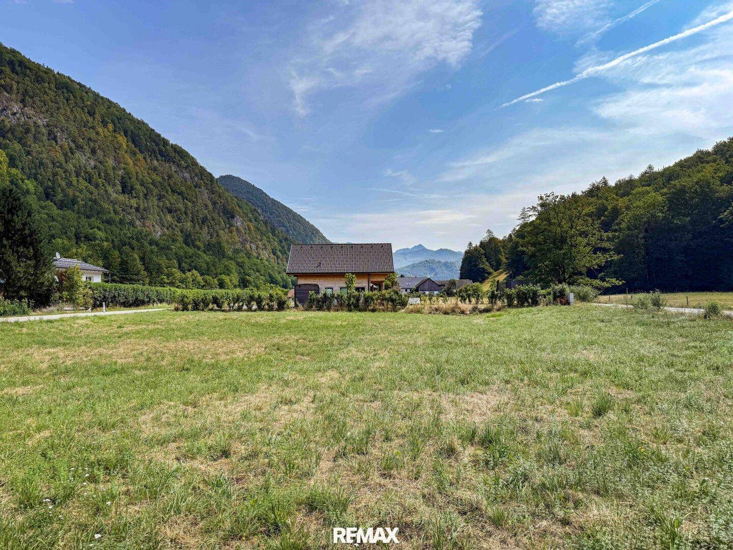 Weitläufiges Wiesengrundstück mit einem charmanten Haus im Hintergrund, umgeben von einer idyllischen Bergkulisse.
